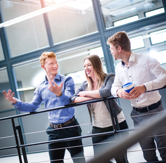 Drei Auszubildende im Gespräch auf der Bürogalerie während einer Besprechung.