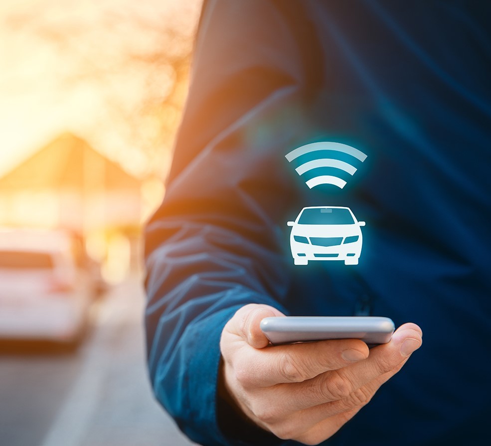 Person hält Handy in der Hand, darüber schwebt Auto und WLAN Symbol. ?>