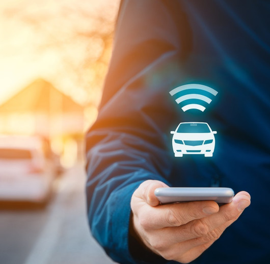 Person hält Handy in der Hand, darüber schwebt Auto und WLAN Symbol.