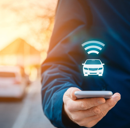 Person hält Handy in der Hand, darüber schwebt Auto und WLAN Symbol.