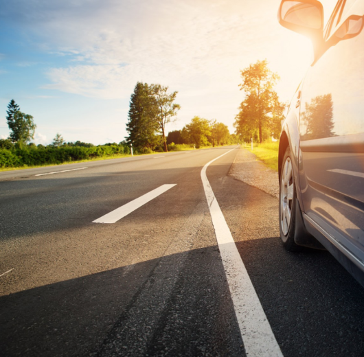 Blaues Auto am Straßenrand bei Sonnenuntergang auf einer leeren Landstraße.