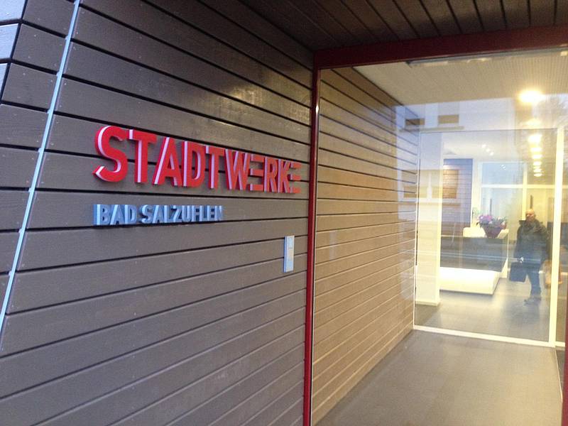 Eingangsbereich der Stadtwerke Bad Salzuflen mit Holzverkleidung und rotem Schriftzug an der Wand, moderne Glasfront. ?>