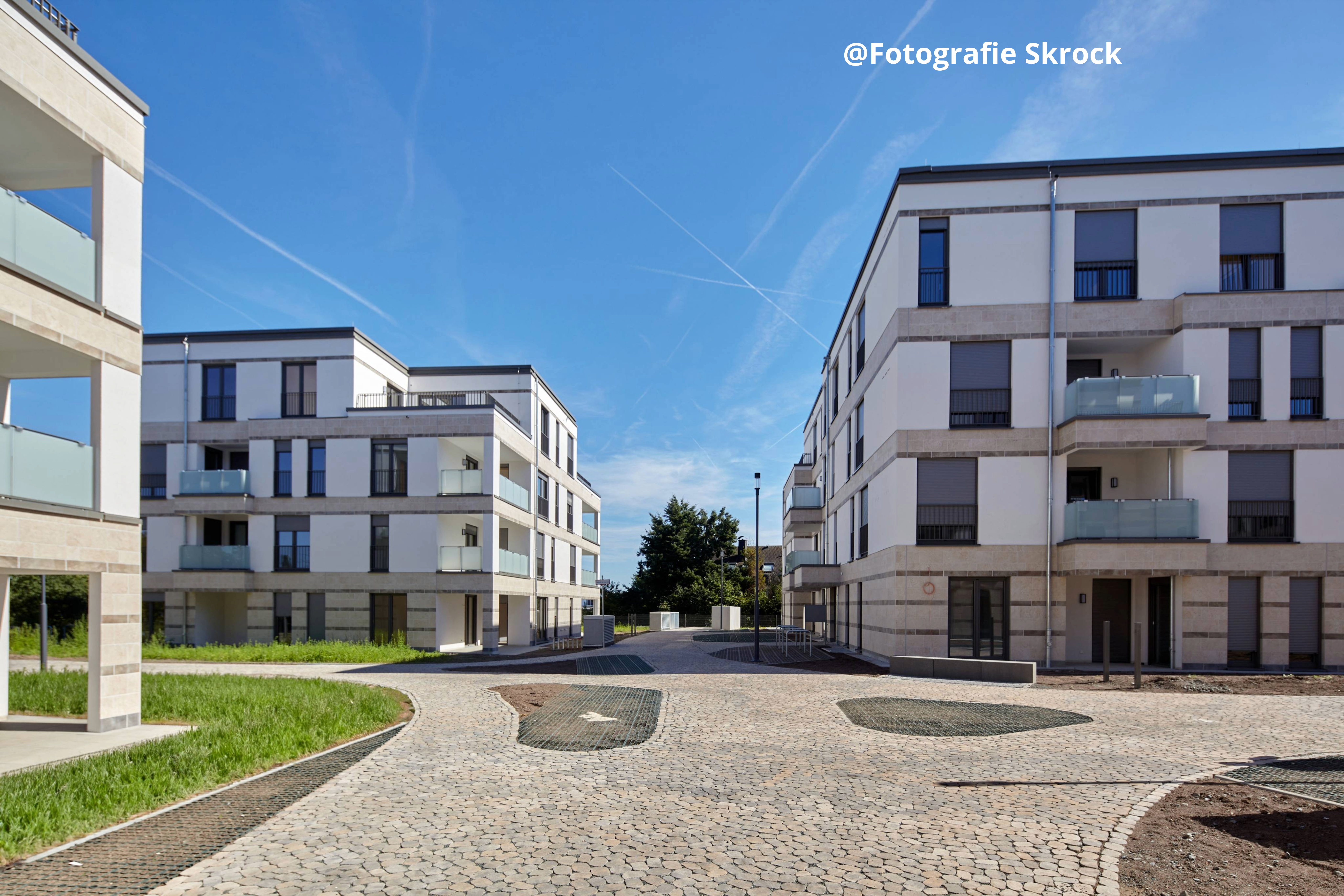 Moderne Wohnanlage mit mehreren mehrstöckigen Gebäuden und gepflastertem Innenhof bei sonnigem Wetter. ?>